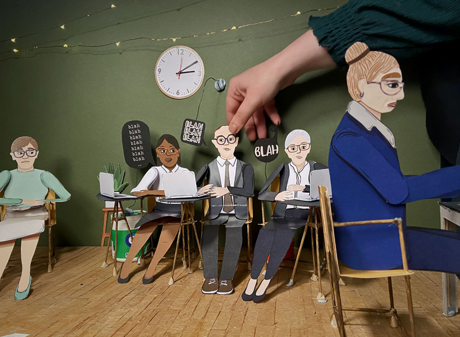 A hand reaching out to touch a paper cut-out of people sitting around a desk.